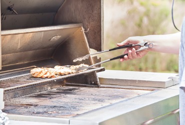 someone cooking chicken on a propane grill in the summer