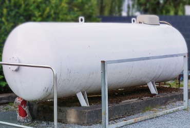 White propane tank outside with trees in the background for Propane Delivery Near Me